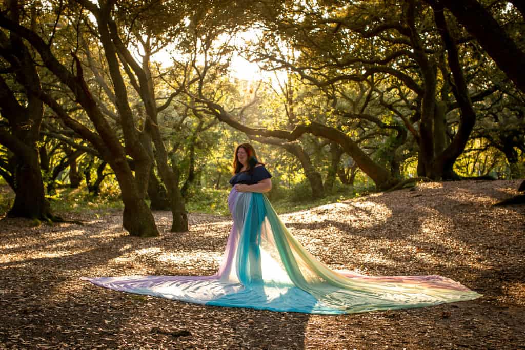 Samantha is standing in a forest of trees waring the rainbow skirt.