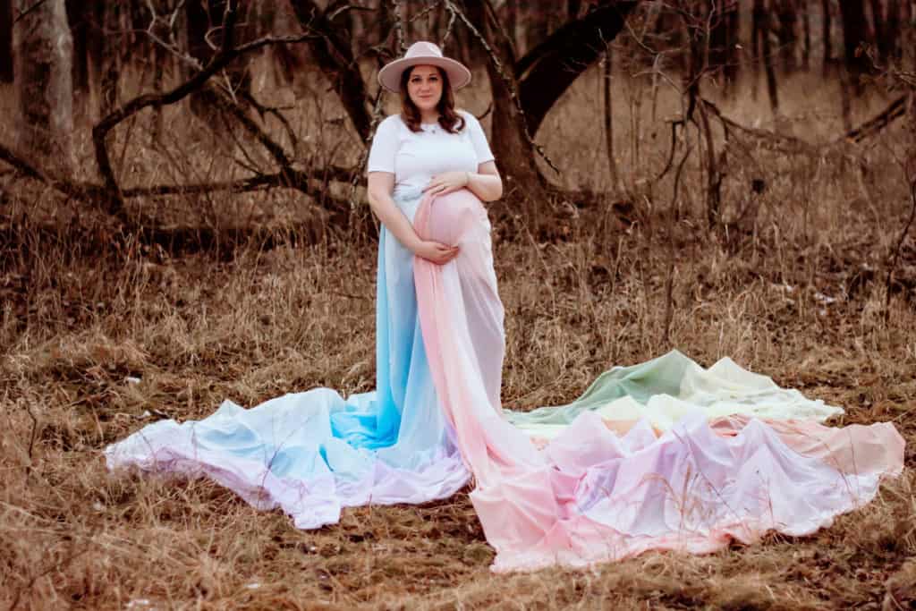 Holly Ann wearing a white top and the rainbow skirt is flowing around her and spread out on the ground.