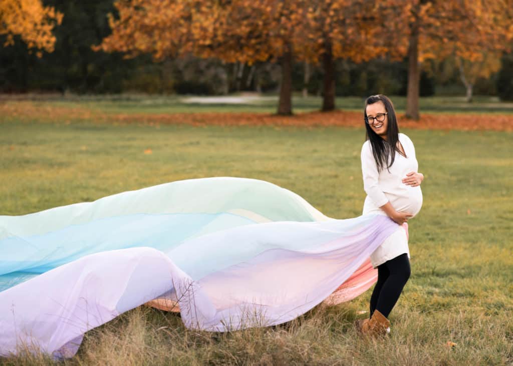 Liana is wearing a white dress and black pants. The rainbow skirt flows out behind her.