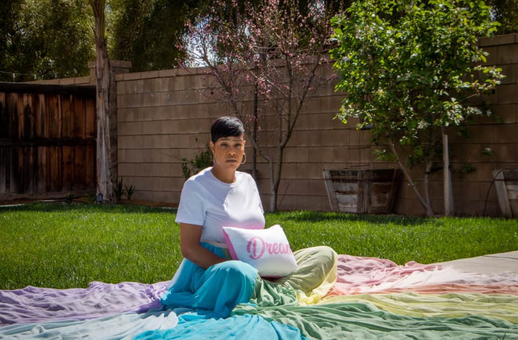 Marsay is sitting on a path with grass on both sides.  The rainbow skirt is spread around her in a circle.  She is holding a pillow with the word "Dream" on it.