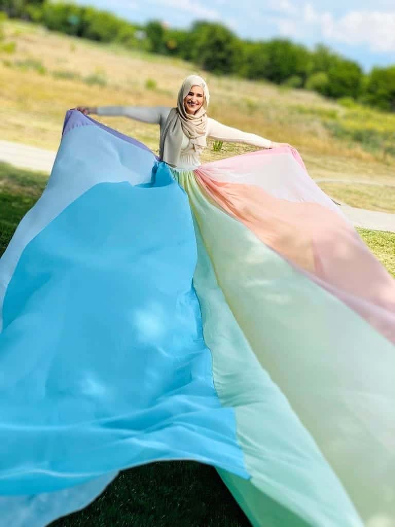 Khadijah holding the rainbow skirt with both arms up into the air. It is flowing out in front of her.