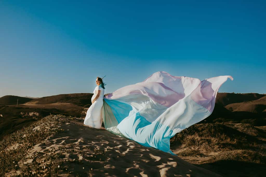 Robin wears a white dress and the rainbow skirt that flows out behind her.