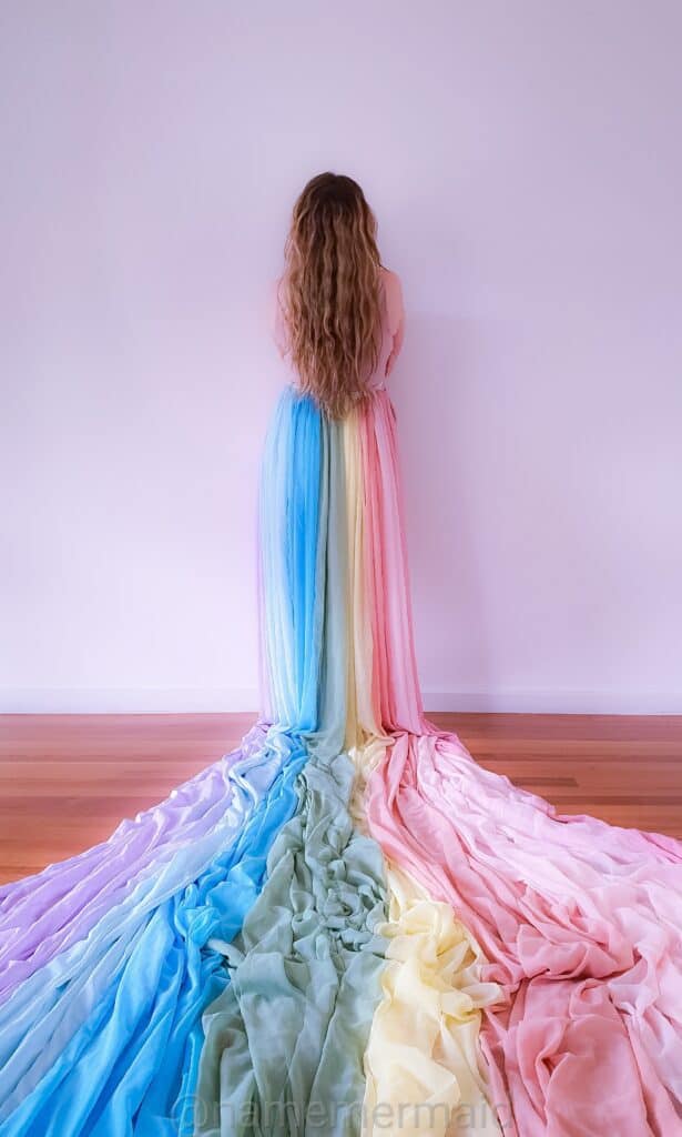 Mimi faces away from the camera. She wears a pink top and the rainbow skirt. The skirt flows out behind her.