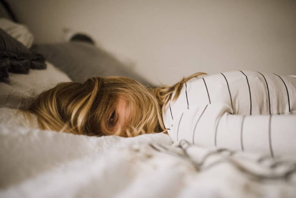 Woman lays face down on bed looking tired.