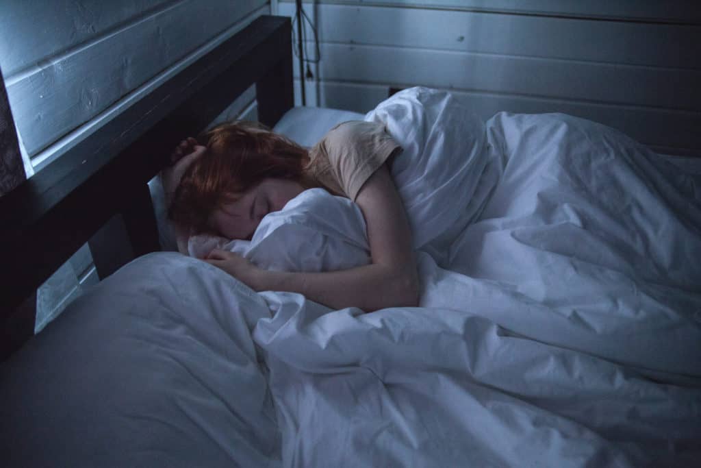 A woman is laying in bed sleeping. She is curled up in the white blankets.