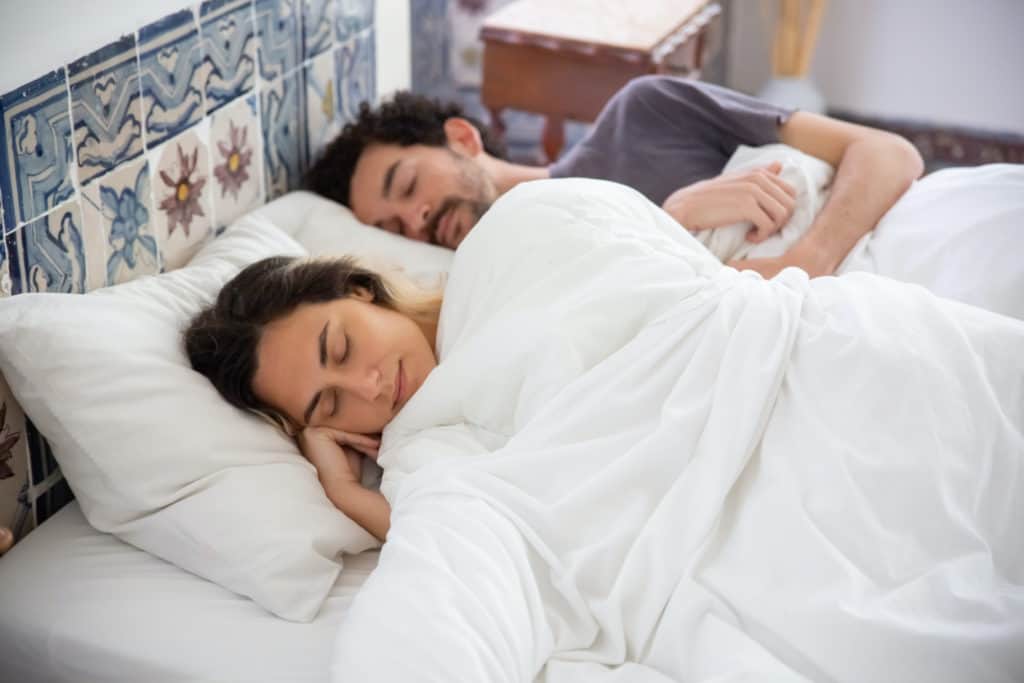 A man and a woman are sleeping next to each other in bed dreaming.