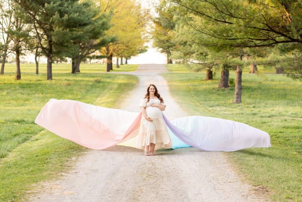 Laura stands on a dirt path surrounded by trees.  She wears the rainbow skirt, which flows out all around her.