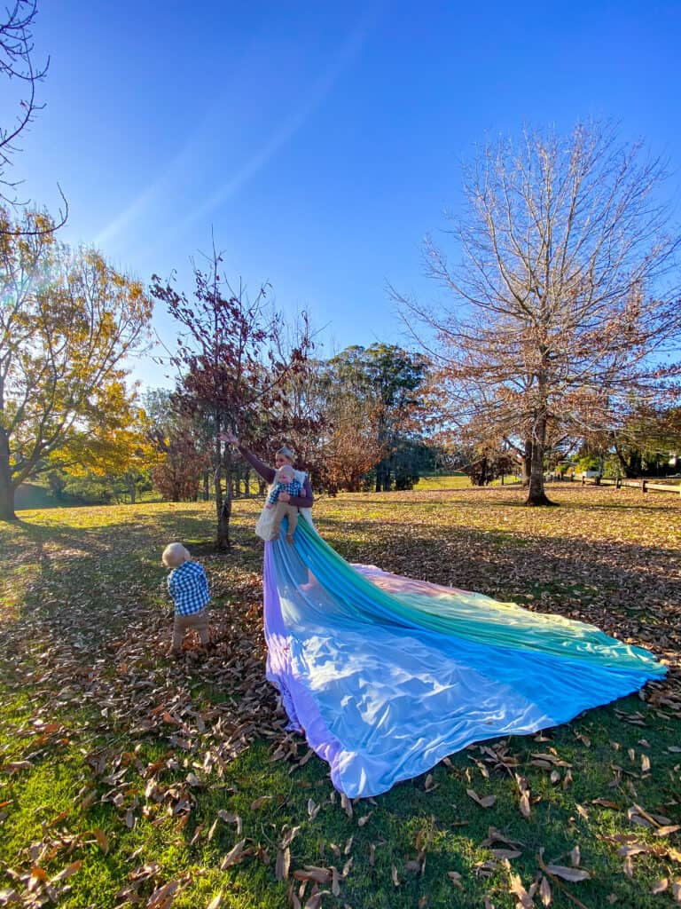 Samantha wears the rainbow skirt. She holds her young son in her arms. Her other son stands next to her on the ground.