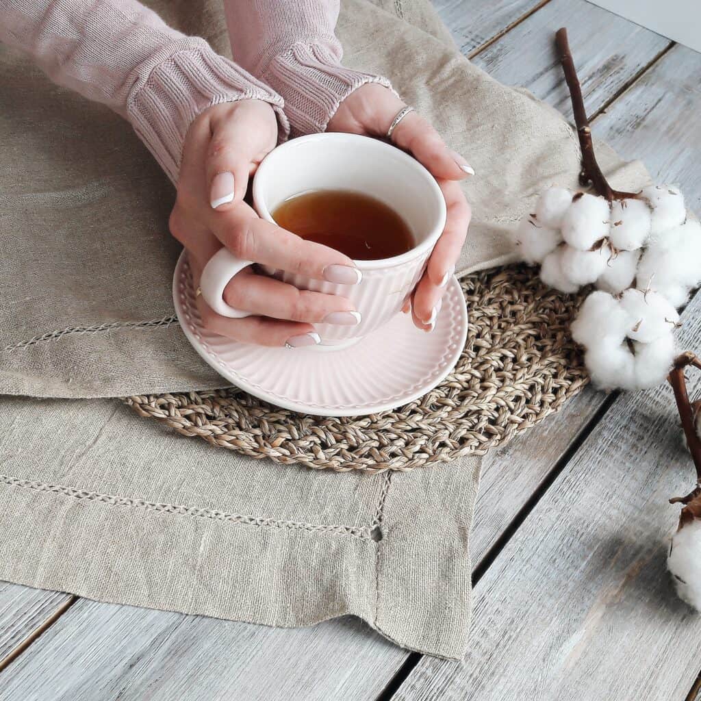 A pair of women's hands holds a cup of hot tea.