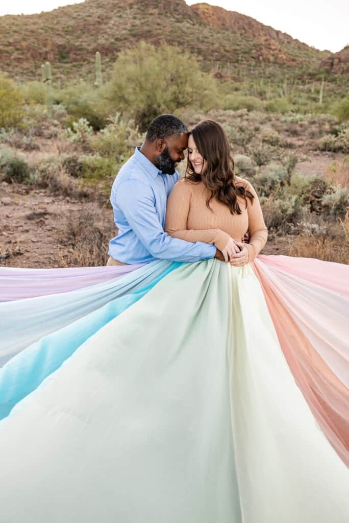 Alex wears the rainbow skirt. It is spread out all around here. Her husband stands next to her, hugging her.