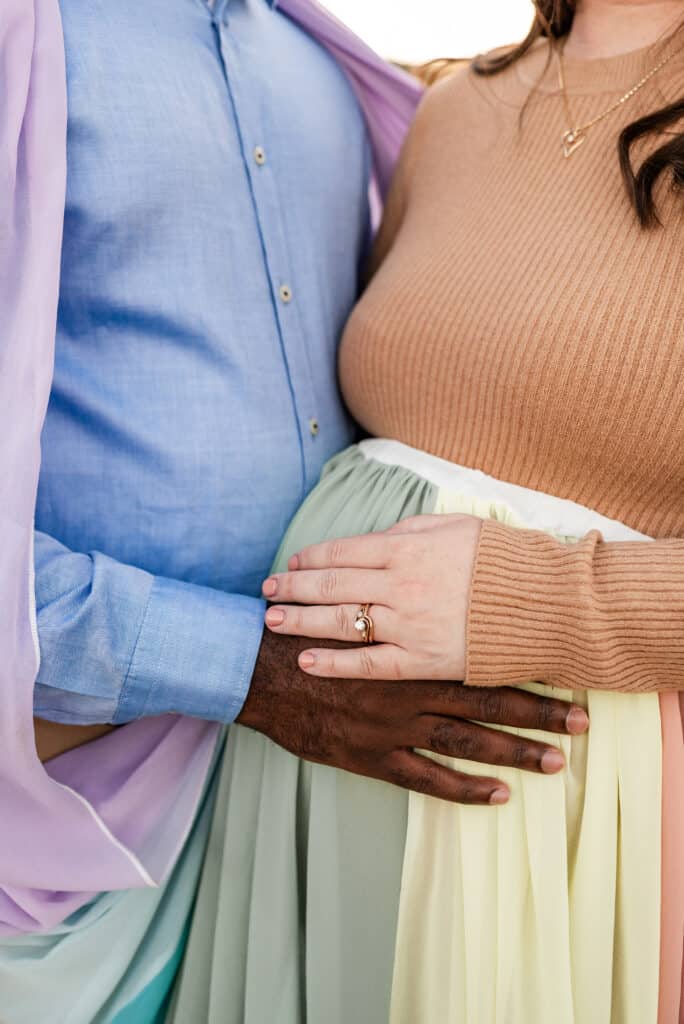 Alex and her husband each rest a hand on her pregnant belly. She wears the rainbow skirt.
