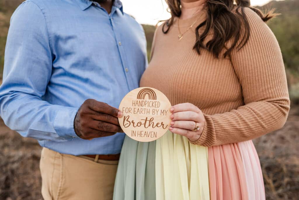 Alex wears the rainbow skirt. She and her husband each hold one side of a sign that says "handpicked for eart by my brother in heaven."
