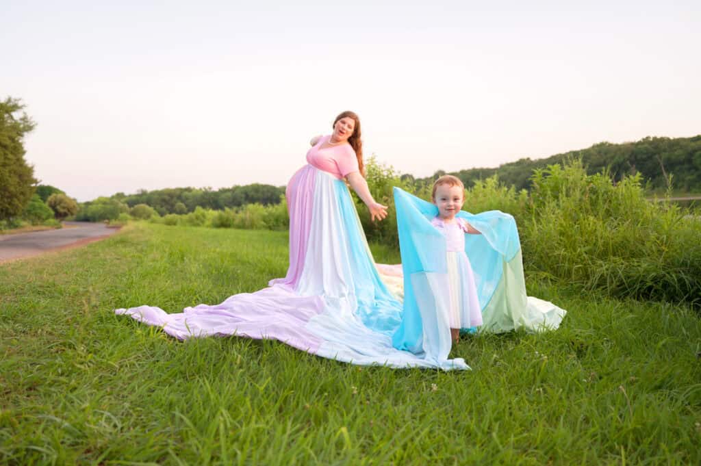 Rachael wears a pink dress and the rainbow skirt. Her daughter wears a rainbow dress and holds the skirt over her shoulders.